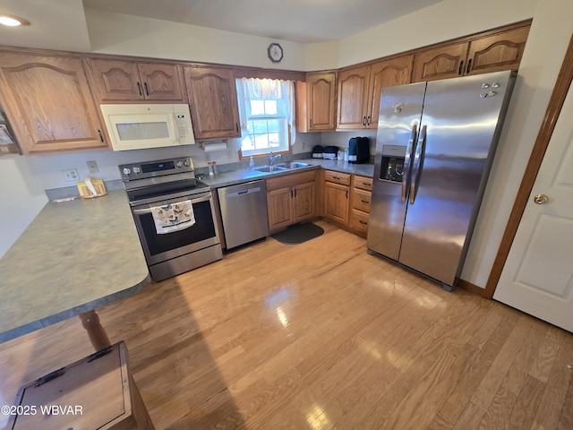 kitchen with light wood finished floors, brown cabinets, appliances with stainless steel finishes, and a sink