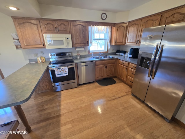 kitchen featuring dark countertops, brown cabinets, appliances with stainless steel finishes, light wood-style floors, and a sink