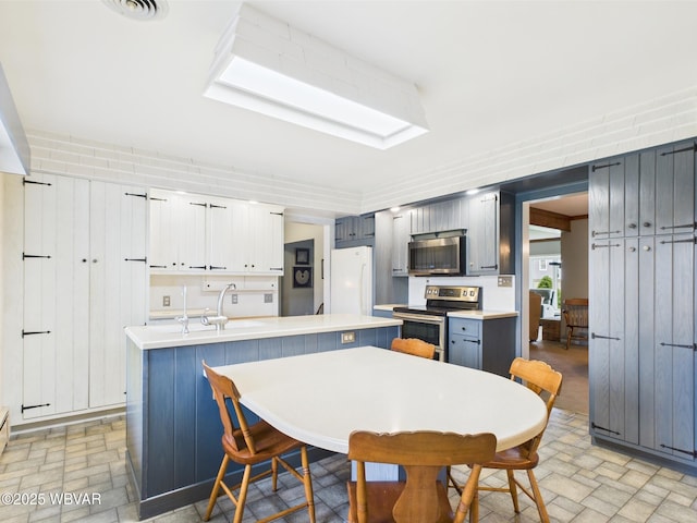 kitchen featuring stainless steel appliances, brick patterned floors, light countertops, and a sink