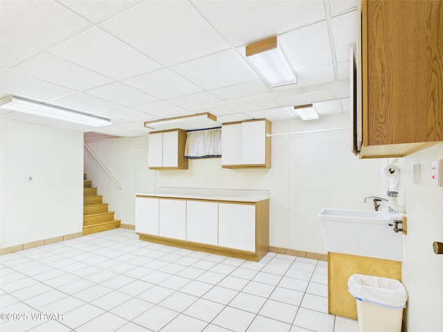finished below grade area with a drop ceiling, stairway, light tile patterned floors, and baseboards