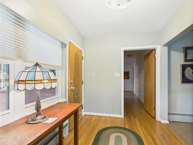 corridor with a baseboard radiator, light wood-style flooring, and baseboards