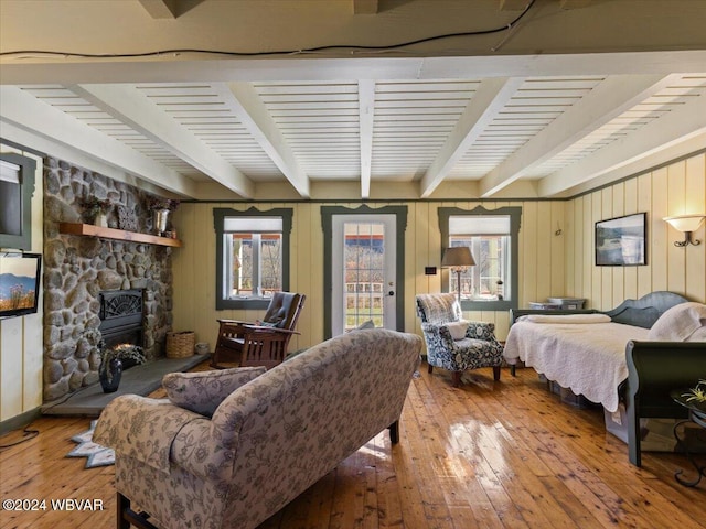 bedroom featuring beam ceiling, a stone fireplace, wood-type flooring, and access to outside