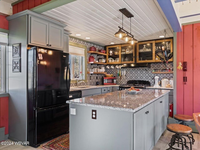 kitchen with a center island, black fridge, hanging light fixtures, gray cabinets, and stainless steel range