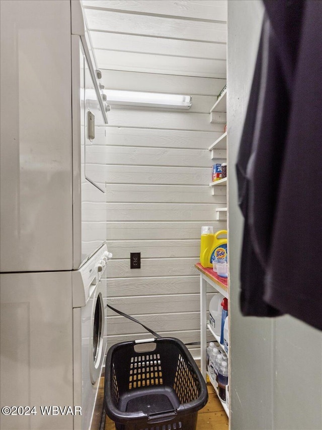 clothes washing area featuring stacked washer / drying machine, wood-type flooring, and wooden walls