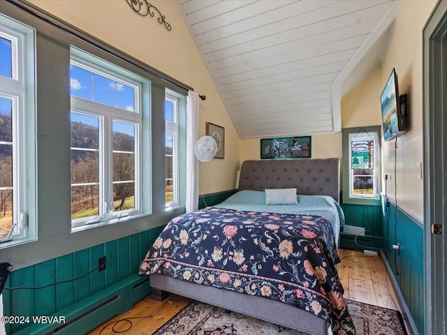 bedroom featuring wood walls, hardwood / wood-style floors, a baseboard radiator, and lofted ceiling