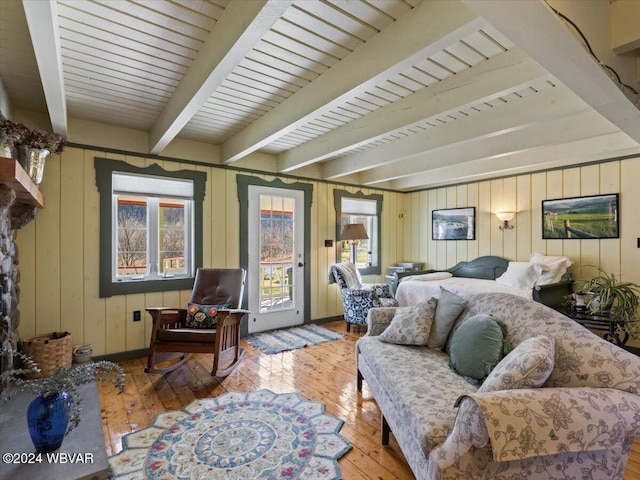 living room with beam ceiling, wooden walls, light hardwood / wood-style flooring, and a healthy amount of sunlight