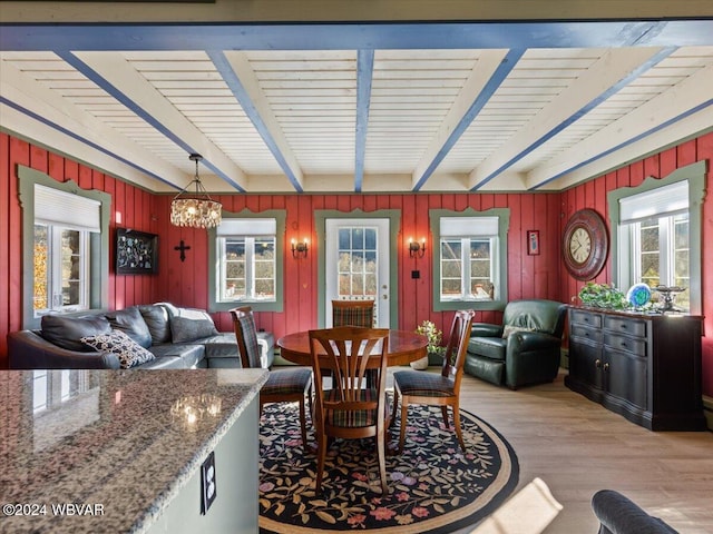 dining space featuring beam ceiling, light hardwood / wood-style floors, an inviting chandelier, and a healthy amount of sunlight