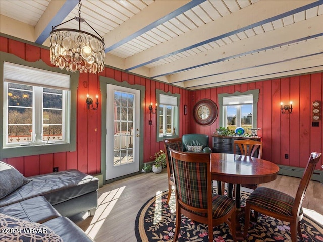 dining room with light wood-type flooring, baseboard heating, wooden walls, an inviting chandelier, and beamed ceiling