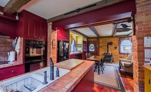 kitchen featuring tile countertops, black appliances, hardwood / wood-style flooring, a wealth of natural light, and beamed ceiling