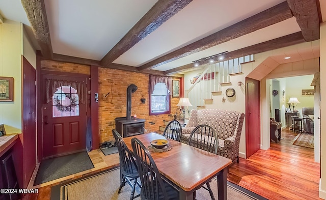 dining space featuring beamed ceiling, a wood stove, brick wall, and light hardwood / wood-style flooring