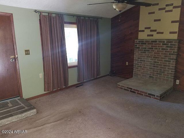 unfurnished living room featuring carpet floors, ceiling fan, and wood walls