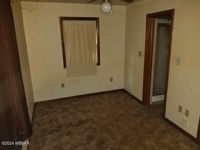 spare room featuring ceiling fan and dark carpet