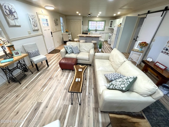 living room with light wood-type flooring, a barn door, and crown molding