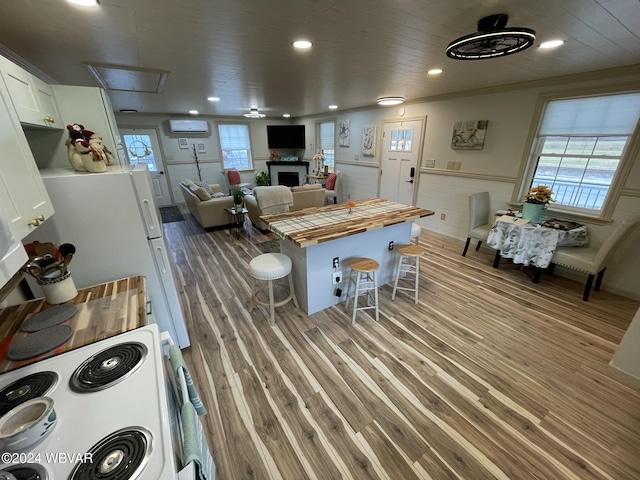 kitchen with hardwood / wood-style floors, white cabinets, white range with electric cooktop, butcher block countertops, and a kitchen bar