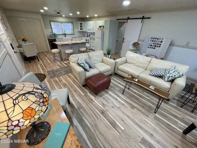 living room featuring a barn door, crown molding, sink, and light hardwood / wood-style floors