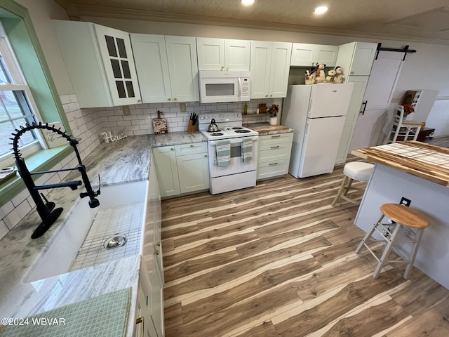 kitchen with a barn door, backsplash, light hardwood / wood-style floors, white appliances, and white cabinets