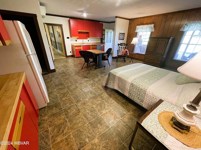 bedroom featuring wood walls, white refrigerator, ornamental molding, and sink