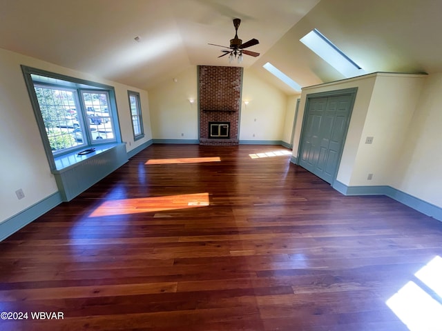 unfurnished living room with ceiling fan, lofted ceiling with skylight, dark wood-type flooring, and a brick fireplace