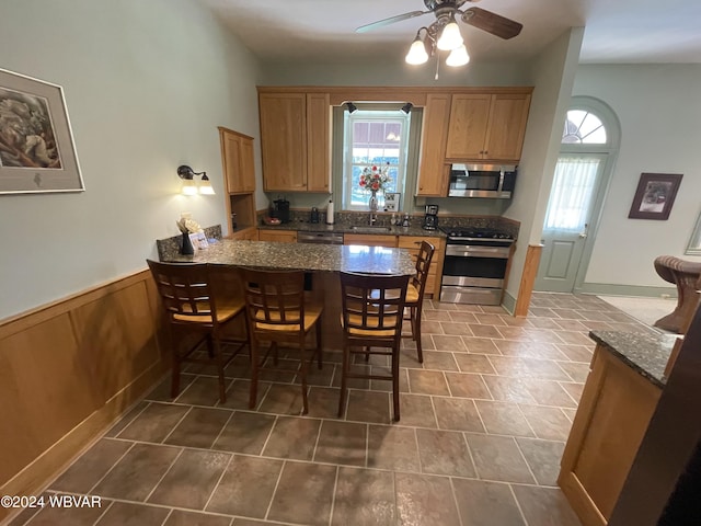 kitchen featuring kitchen peninsula, dark stone counters, stainless steel appliances, ceiling fan, and sink