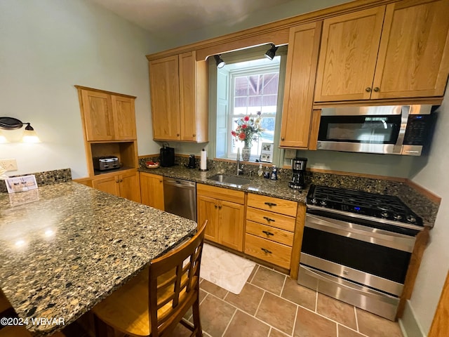 kitchen featuring stainless steel appliances, tile patterned floors, dark stone countertops, and sink