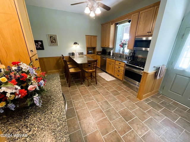 kitchen with wood walls, sink, dark stone counters, and appliances with stainless steel finishes