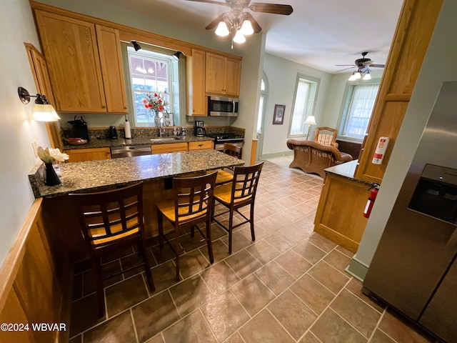 kitchen with sink, tile patterned flooring, ceiling fan, dark stone countertops, and stainless steel appliances