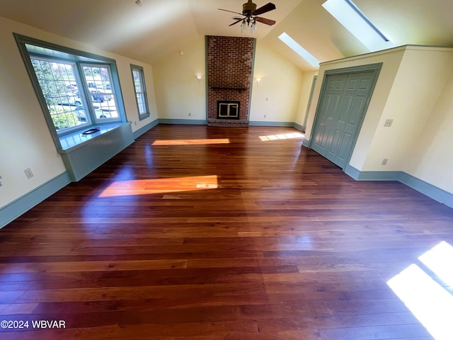 unfurnished living room featuring ceiling fan, vaulted ceiling with skylight, dark hardwood / wood-style floors, and a brick fireplace