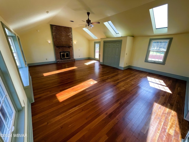 unfurnished living room with dark hardwood / wood-style flooring, a brick fireplace, ceiling fan, and vaulted ceiling with skylight