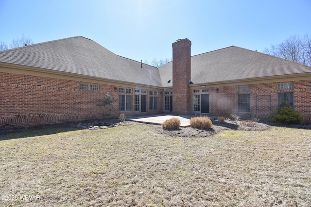 rear view of house featuring a lawn, brick siding, a chimney, and a patio area