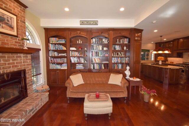 living area with dark wood-style floors, recessed lighting, and a brick fireplace