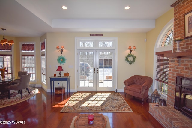 interior space with a brick fireplace, baseboards, wood finished floors, recessed lighting, and french doors