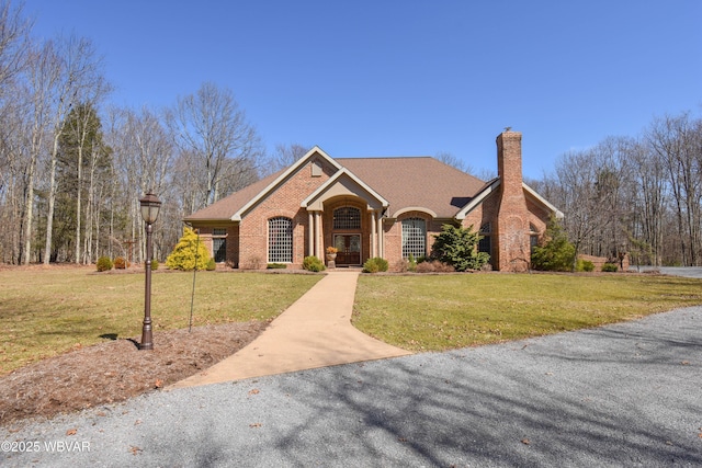 view of front of house with a shingled roof, a chimney, a front yard, and brick siding