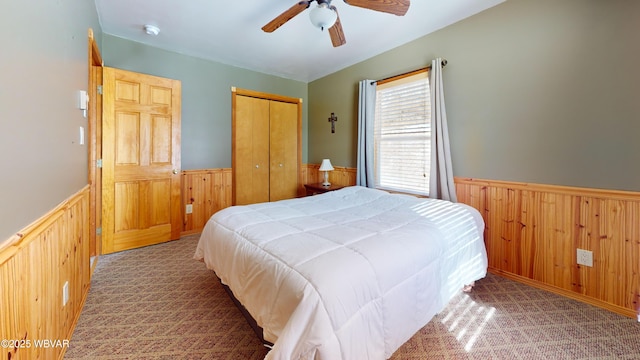 bedroom featuring ceiling fan, carpet flooring, wooden walls, and a closet