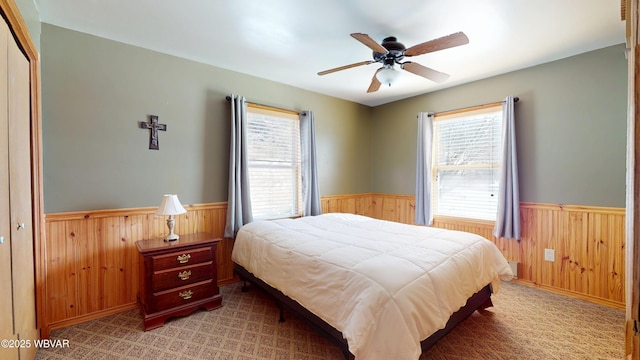 carpeted bedroom with ceiling fan and wood walls