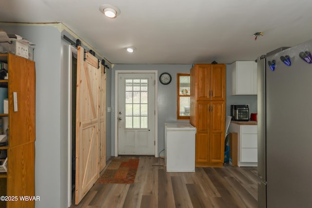kitchen featuring wood finished floors, fridge, a barn door, freestanding refrigerator, and brown cabinets