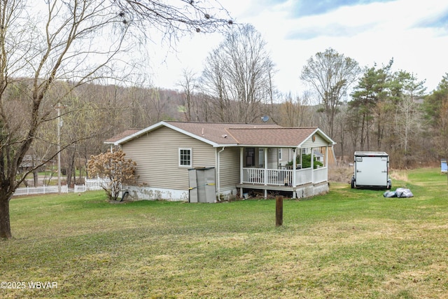 rear view of house with a forest view, a shingled roof, and a yard
