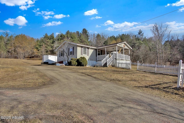 manufactured / mobile home with dirt driveway, fence, a porch, and a forest view