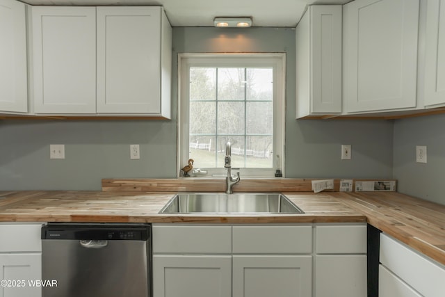 kitchen featuring stainless steel dishwasher, white cabinetry, wood counters, and a sink