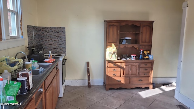 kitchen with sink, white electric range oven, backsplash, dark stone countertops, and light tile patterned floors