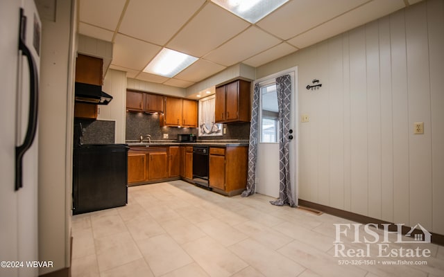 kitchen featuring a paneled ceiling, wood walls, backsplash, white refrigerator, and black stove