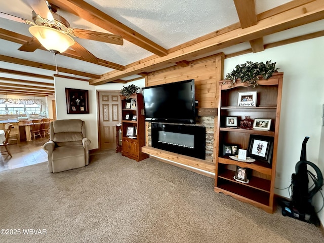 living area with ceiling fan, beamed ceiling, carpet flooring, and a textured ceiling