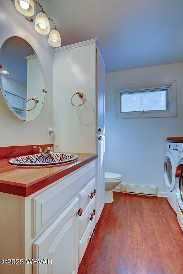 bathroom with toilet, a baseboard radiator, wood finished floors, washing machine and clothes dryer, and vanity