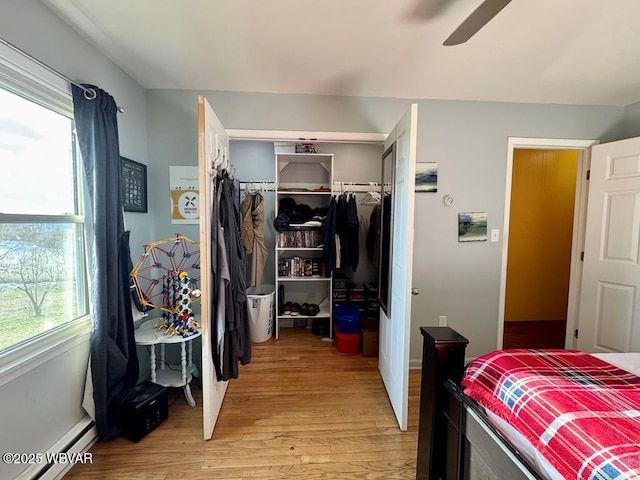 bedroom with light wood finished floors, a baseboard radiator, a ceiling fan, and a closet