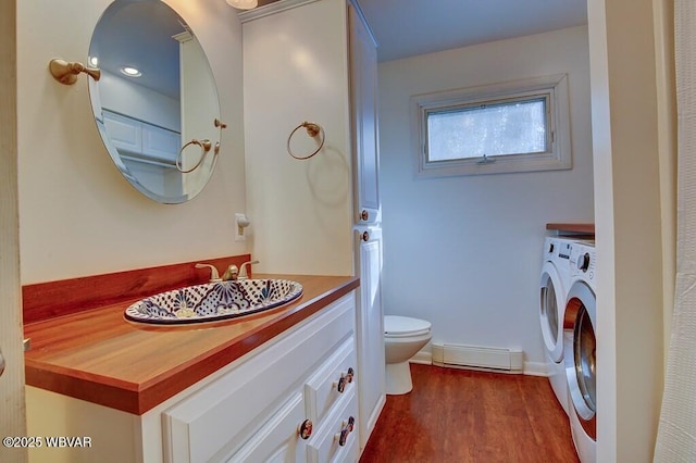 bathroom featuring toilet, a baseboard radiator, wood finished floors, washing machine and clothes dryer, and vanity