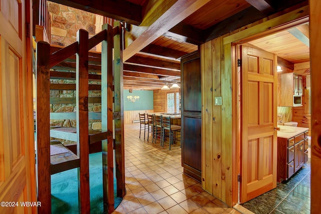 hall with wooden ceiling, wood walls, tile patterned flooring, and beamed ceiling