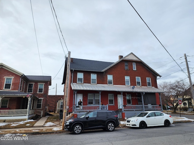 townhome / multi-family property with covered porch, brick siding, and a chimney