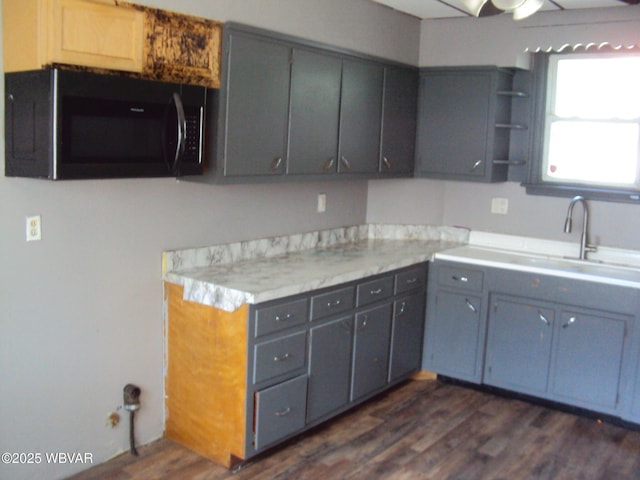 kitchen with light countertops, gray cabinets, dark wood finished floors, and a sink