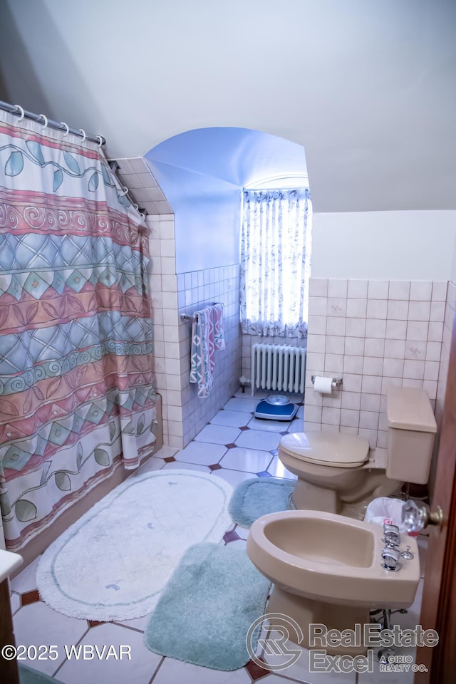 bathroom with radiator heating unit, tile walls, tile patterned flooring, toilet, and a bidet