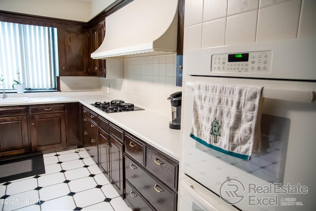 kitchen with premium range hood, dark brown cabinets, oven, and black gas stovetop