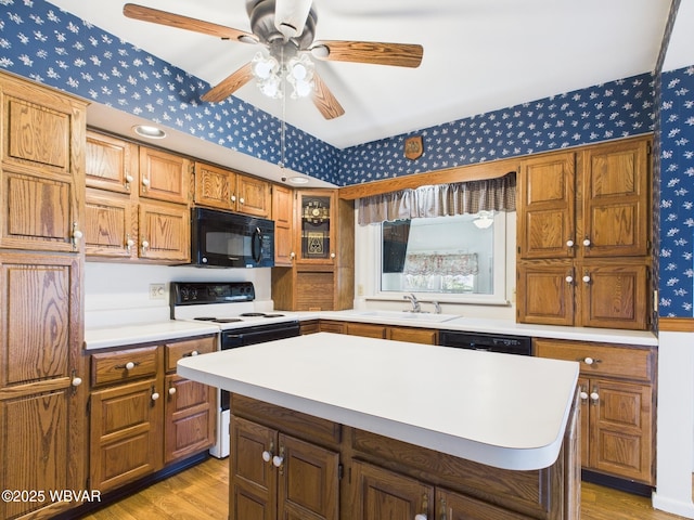 kitchen featuring wallpapered walls, light wood finished floors, light countertops, black appliances, and a sink